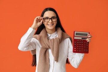 Beautiful young woman with calculator on orange background