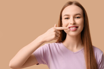 Young woman pointing at her teeth on beige background