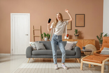 Young pretty woman dancing with mobile phone in stylish living room
