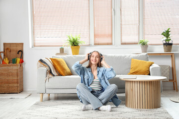 Young pretty woman in headphones listening music on floor in light living room