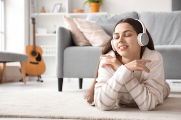 Beautiful young happy woman in headphones listening music and lying on floor at home
