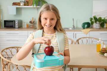 Happy girl with school lunchbox and fresh apple in kitchen