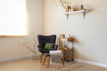 Stylish living room with black armchair, shelf and vase with blooming branches