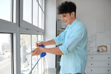 Young man cleaning window with squeegee at home