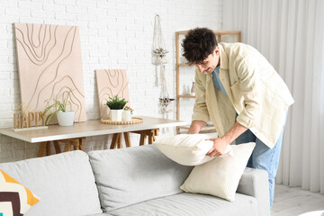 Young man adjusting sofa cushions at home