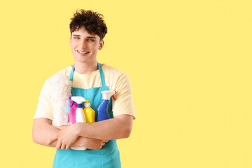 Male janitor with bottles of detergent on yellow background