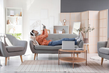 Young tattooed man in headphones with mobile phone listening to music on sofa at home