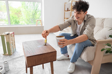 Young man painting wooden table at home