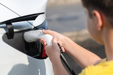 Kid's hand insert EV charger plug into electric vehicle, recharge EV car battery from outdoor...
