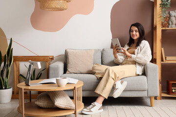 Young woman using tablet computer on grey sofa at home