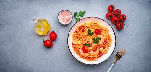 Cooked Italian spaghetti pasta with shrimp and tomato sauce, gray table background, top view banner