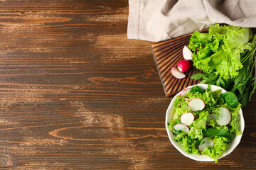 Bowl of tasty salad with radish on wooden background
