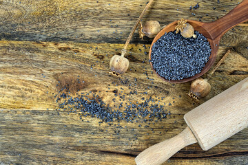 Poppy seeds and several dried poppy seed pods on wooden table
