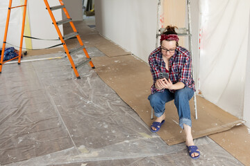 A woman in jeans sits in a paint-protected room and studies a video tutorial on how to carry out renovations. High quality photo