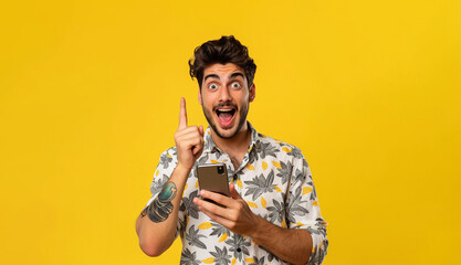 A man is holding a cellphone with finger pointing to the top, an excited expression, wearing a floral shirt and has tattoos on his arm on yellow background 