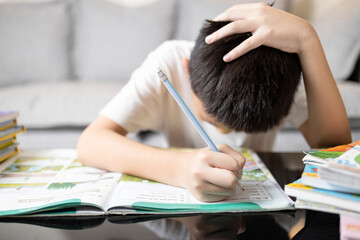 Asian kid boy holding head in hand,schoolboy study hard,tired from studying,Stressed male student while doing homework,child experienced difficulties in learning,health care and education concept