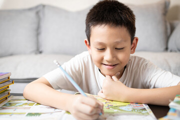 Happy asian kid boy concentrating on studying,focused attention,writing and reading a book,serious male student doing homework alone at home,elementary child schoolboy eager to learn,education concept