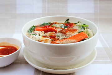 Boil shredded pork Fish sticks, chicken eggs, glass noodles, many types of vegetables, topped with dipping sauce. In a cream-colored ceramic bowl with a saucer.

