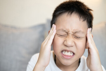 Sick child boy suffering from severe headache,holding his head,tension or migraine headache in...