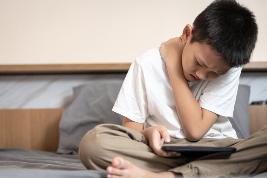 Asian boy suffering from neck muscle and shoulder pain,aching in spinal back,sitting and bending his back,poor posture,tilting his head down long time while playing game on mobile phone,bad position