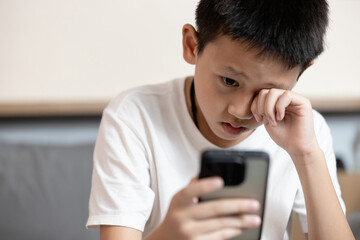 Asian child boy overusing his smart phone,addicted to mobile phone,game addiction,effects on young children's brains,disease of ADHD,Nomophobia,dry eyes,eyesight problems,loss of vision,health care © Satjawat