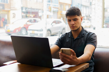 A man is sitting at a table with a laptop and a cell phone