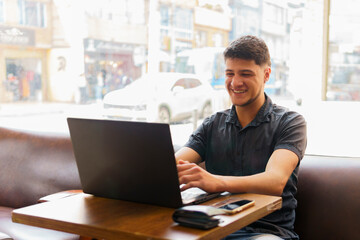 A man is sitting at a table with a laptop and smiling