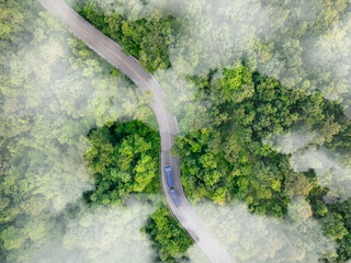 Aerial view of hydrogen energy truck driving on highway road in green forest. Sustainable transportation. Blue truck driving on asphalt road in forest. Hydrogen fuel cell vehicle. Zero emission car.