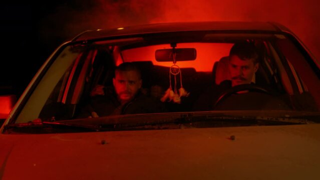 Two men pulling ski masks over their faces and getting out of a car