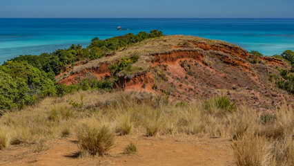 The amazing landscape of Madagascar. The red-soil hill is covered with dry grass and green shrubs....