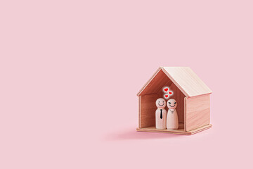 Happy wooden male and female figures inside a tiny wooden house isolated on a pink background. The couple smiling and stand close together