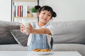 A young girl is holding a glass of milk and a plate of cookies