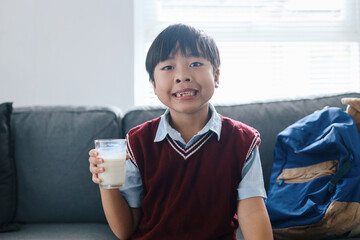 Healthy schoolboy in uniform drinking glass of milk for breakfast before go to school.