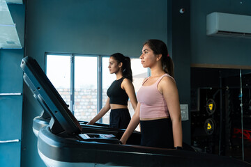 Two Fit adult indian girls 20s exercise on treadmills at gym. women jogging healthy Fitness...
