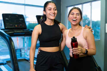 Two happy young fit indian friends women holding water bottle relaxing after workout at fitness...