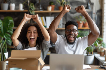 Excited young African American couple celebrating success with raised arms in front of their computer in a cozy home office. - Powered by Adobe