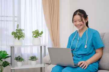 A young Asian female nurse wearing a green medical uniform works typing on a laptop sitting on a...