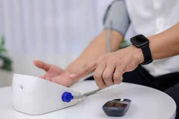 Close-up of an Asian senior man with diabetes and high blood pressure test results, using a blood pressure monitor to check himself and preventing diabetes and high blood pressure at home.