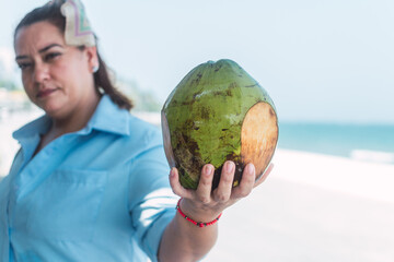 Latin woman drinking coconut water on the beach, at a street stall with glasses of tropical fruits.