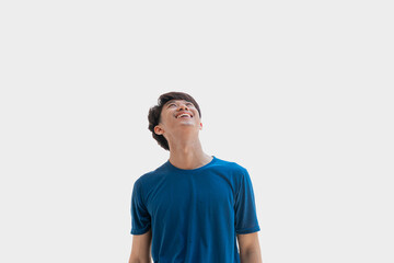 A young Asian man in his 20s wearing a blue t-shirt stands looking above, isolated on a gray background. Positive person