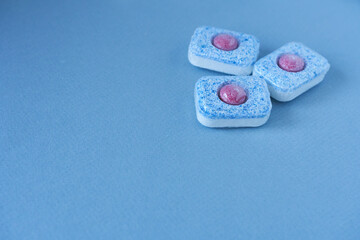 Close-up of blue and pink dishwasher tablets on blue background with copy space.