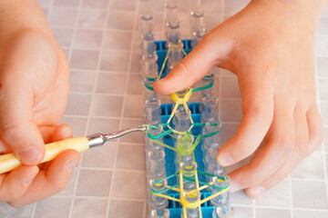 輪ゴムの編み機でゴムを編んでいる小学4年生の女の子の手元。