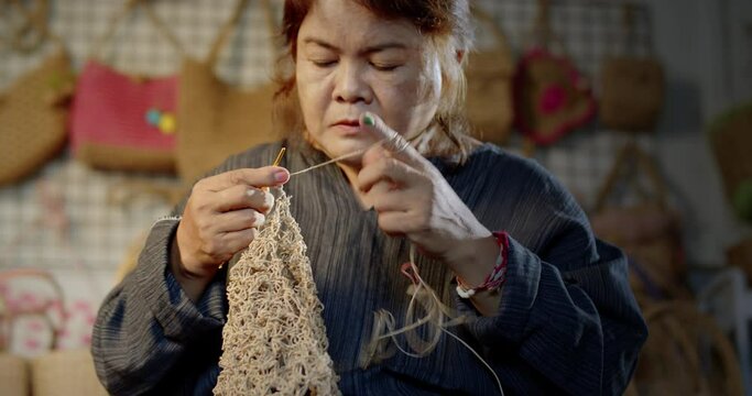 Slow motion scene while an Asian female artisan who is a local villager knitting folk basket made from leftover paper band to sell as extra income in the basketry shop shop.