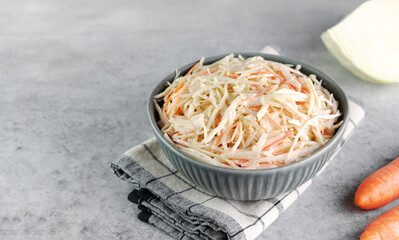 Classic coleslaw salad made with fresh cabbage, carrots and dressing on a gray background. American...