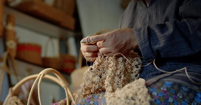 Slow motion scene while an Asian female artisan who is a local villager knitting folk basket made from leftover paper band to sell as extra income in the basketry shop shop.
