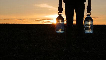 A man holds two bottles of drinking water, stands in a field at sunset