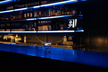 A bar with a blue counter and shelves of liquor. The bar is empty and the lights are on.