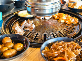 Experience the flavors of Korea in this picture of a samgyupsal restaurant with various BBQ meats, side dishes, and a sizzling grill.