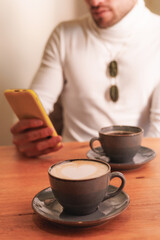Unrecognizable latin man using cellphone in a coffee shop. Vertical view. Coffee in the foreground.