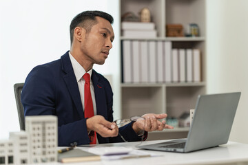 Confident professional businessman presents a client with a condominium building model offering new real estate to potential buyers via laptop online.